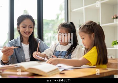 Zwei süße kleine asiatische Mädchen konzentrieren sich darauf, mit einer Privatlehrerin zu Hause zu lernen und Hausaufgaben zu machen. Kindererziehungskonzept Stockfoto