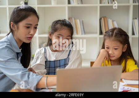 Zwei glückliche und süße junge asiatische Mädchen lernen zu Hause mit einem Privatlehrer und lernen gemeinsam eine Lektion auf einem Laptop. Stockfoto