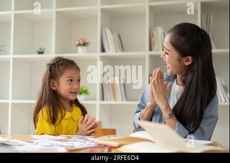 Eine fürsorgliche und freundliche asiatische Lehrerin klatscht mit einem kleinen Mädchen in die Hände, ist stolz auf ihre Schülerin und genießt den Kurs zusammen. Stockfoto