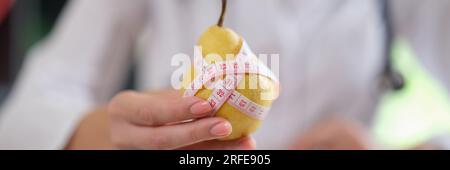 Ernährungswissenschaftler zeigt reife gelbe Birne mit Maßband, während er in der Arztpraxis sitzt. Stockfoto