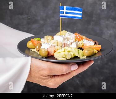 Weibliche Hände servieren einen Teller mit köstlichem griechischen Salat mit Fetakäse und Oliven Stockfoto