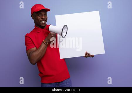 Ein junger amerikanischer Mann in Baseballmütze und T-Shirt-Uniform, der die Nachrichten auf einem Poster berichtet Stockfoto