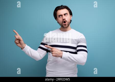 Charmanter positiver 30er-Jahre-Mann in rotem Hemd, der mit dem Finger zur Seite zeigt Stockfoto