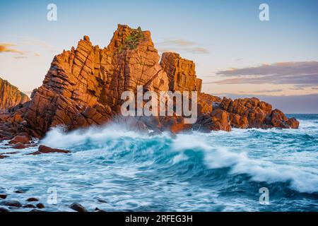 Große Wellen schlagen gegen Felsformationen an der Küste, die von goldenem Abendlicht am Cape Woolamai, Phillip Island, Victoria, Australien gefärbt sind Stockfoto