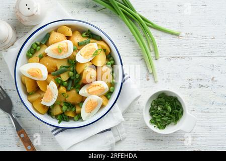 Traditioneller Kartoffelsalat mit Speck und Eiern in einer weißen Schüssel. Picknick-Food-Konzept. Schüssel mit warmem Kartoffelsalat. Deutscher Kartoffelsalat. Draufsicht. Stockfoto