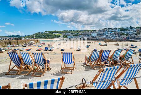 Die Liegestühle stehen am Meer am Hafen von St. Ives in Cornwall, Großbritannien, in Schlange Stockfoto