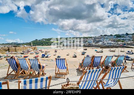 Die Liegestühle stehen am Meer am Hafen von St. Ives in Cornwall, Großbritannien, in Schlange Stockfoto