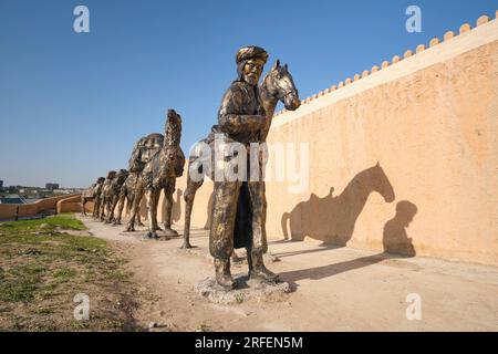 Eine große Bronzeskulptur mit einer typischen Seidenstraße-Karawane mit Kamelen und Pferden, die Güter durch die Wüste transportieren. In der alten Festung, Cit Stockfoto