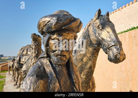 Eine große Bronzeskulptur mit einer typischen Seidenstraße-Karawane mit Kamelen und Pferden, die Güter durch die Wüste transportieren. In der alten Festung, Cit Stockfoto