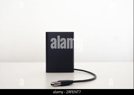 Schwarzes mobiles Ladegerät auf dem Tisch mit einem schwarzen isolierten usb-Kabel. Weißer Hintergrund. Stockfoto