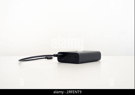 Schwarzes mobiles Ladegerät auf dem Tisch mit einem schwarzen Anschlusskabel: usb Typ c. Weißer Hintergrund. Stockfoto