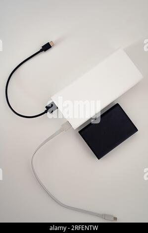 Schwarze Powerbank parallel zum weißen mobilen Ladegerät mit weißem und schwarzem Kabel, das mit dem zweiten Gerät verbunden ist. Weißer Hintergrund. Stockfoto