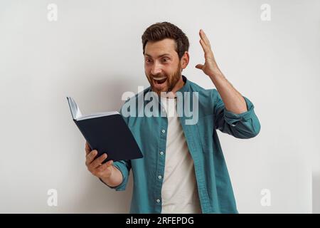 Der inspirierte Mann hält ein offenes Notizbuch in den Händen und macht aktiv Gesten Stockfoto