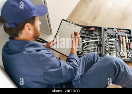 Rückansicht eines professionellen Handwerkers mit offener Werkzeugtasche auf dem Boden der Küche Stockfoto