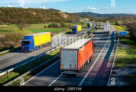 Transportwaggons in Schlangen, die auf einer Landstraße unter einem wunderschönen blauen Himmel vorbeifahren Stockfoto