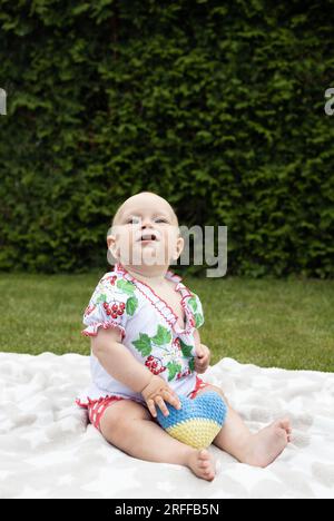 Ein kleines Mädchen in einer bestickten Bluse sitzt auf dem Gras. Kinder werden gebeten, den Krieg in der Ukraine zu beenden. Flüchtlinge mit Liebe zur Ukraine. Unabhängigkeitstag. Stockfoto