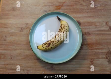 Nahaufnahme einer fleckigen gelben Banane auf einem Teller auf einem hölzernen Schneidebrett. Stockfoto