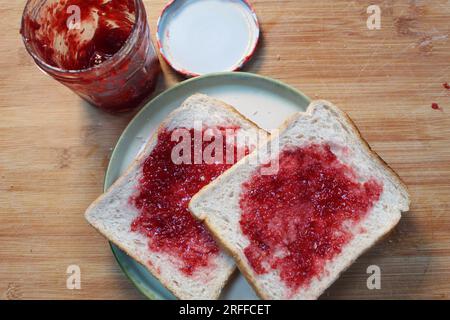 Ein Foto von zwei Brotstücken mit Marmelade und einem Marmeladenglas daneben. Stockfoto