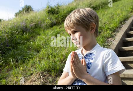 7-jähriger Junge in einem Vishyvanka, Hände gefaltet im Gebet, ein Appell an Gott. Träume vom Frieden für die Heimat Ukraine. Kinder sollen den Krieg beenden Stockfoto