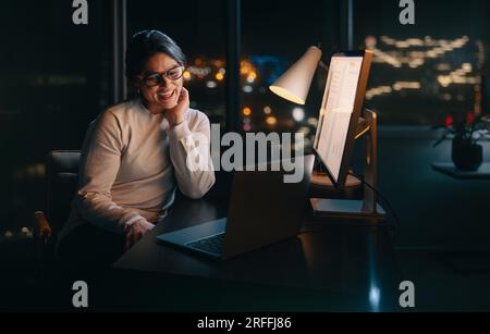 Geschäftsfrau sitzt an ihrem Schreibtisch und nimmt an einem virtuellen Meeting außerhalb der Geschäftszeiten Teil. Mit einem Laptop kommuniziert sie per Videoanruf, ein Beispiel für p Stockfoto