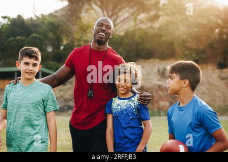 Der Trainer der Grundschule steht mit seinem Footballteam auf einem Feld. Sportlehrer, der eine Gruppe von Kindern in der Grundschule ausbildet. Mentorenstudium A Stockfoto