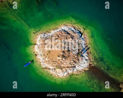 Drohnenfoto von Mann beim Stand-Up-Paddle-Boards SUP. Kleine felsige Insel im Kapchagay-See in Kasachstan bei Sonnenuntergang. Stockfoto