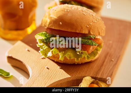 Gesunde Alternative klassischer amerikanischer Hamburger - Fischburger mit Lachs, Gurken, Tomaten und Salat unter harten Schatten. Stockfoto