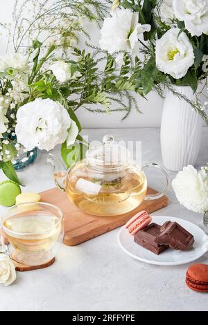 Tischeinstellung am Morgen. Grüner Tee, Makronen-Desserts, Schokolade, weiße Blumen - Zeit für sich, genießen Sie Ihr Zeitkonzept. Stockfoto