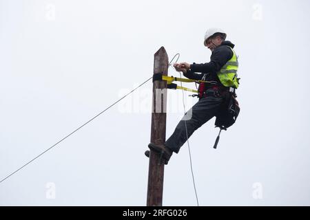 Techniker, der ein Breitband-Glasfaserkabel an einen Pol anschließt Stockfoto