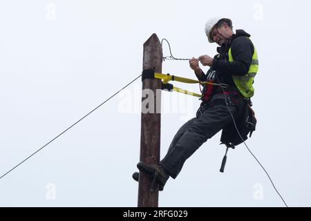 Techniker, der ein Breitband-Glasfaserkabel an einen Pol anschließt Stockfoto