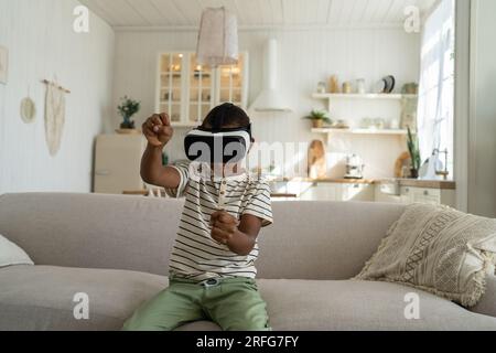 Fokussierter afroamerikanischer Junge fährt Auto und spielt Rennvideospiel in einem Virtual-Reality-Headset. Stockfoto