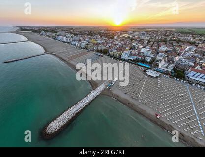 Drohnenfoto der Küste von Caorle, Venedig, Italien bei Sonnenuntergang. Regenschirme in der Stadt des County Resorts Stockfoto