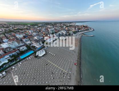 Drohnenfoto der Küste von Caorle, Venedig, Italien bei Sonnenuntergang. Regenschirme in der Stadt des County Resorts Stockfoto