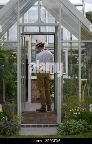 Vertriebsmitarbeiter steht neben Werken im ausgestellten Gewächshaus, Hartley Botanic „Feel Good“-Messestand – RHS Tatton Park Flower Show, 2023, Cheshire England, Großbritannien. Stockfoto