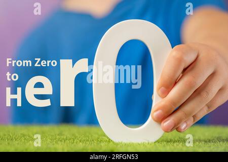 Von Null zu Hero. Nahaufnahme eines Konzeptfotos einer Hand mit einer weißen Null. Motivierender Text, der zu neuen Erfolgen und dem Streben nach Erfolg inspiriert. Stockfoto