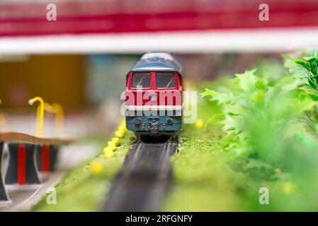 Rotes Lokomotivmodell auf Gleisanordnung mit Bäumen und Brücke Stockfoto