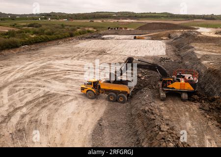 Luftaufnahme direkt über einem Kran oder einem mechanischen Bagger mit Greiferbeladung eines Muldenkippers mit Erde und Erde in der Bauindustrie auf einem Brownfi Stockfoto