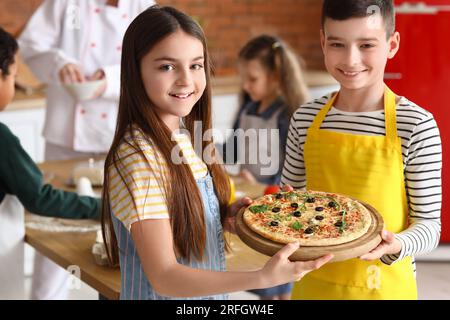 Kleine Kinder mit zubereiteter Pizza nach dem Kochkurs in der Küche Stockfoto