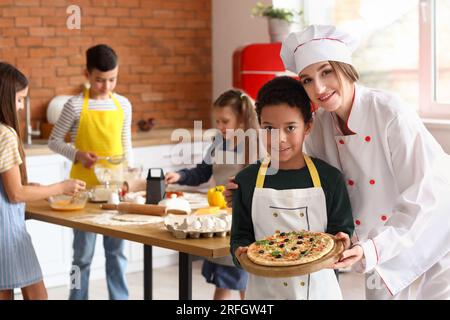 Weiblicher Koch mit kleinem Jungen und nach dem Kochkurs in der Küche zubereitete Pizza Stockfoto