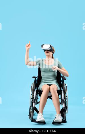 Junge Frau im Rollstuhl mit VR-Brille auf blauem Hintergrund Stockfoto