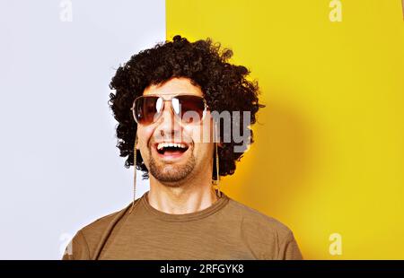 Porträt eines lächelnden bärtigen Mannes mit Kettenbrille, isoliert auf gelbem und weißem Hintergrund Stockfoto