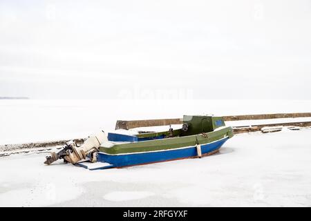 Altes einsames Motorboot in einem gefrorenen Hafen im Winter, verschneite Landschaft, viel Platz zum Kopieren oben Stockfoto