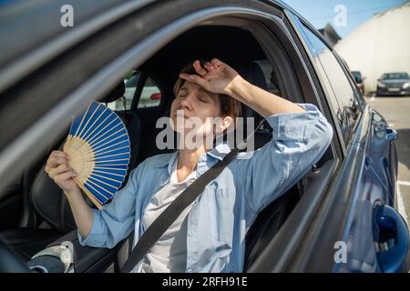 Erschöpfte Frau mittleren Alters fährt Autowellen blauer Fan leidet an Stau im Verkehr. Stockfoto