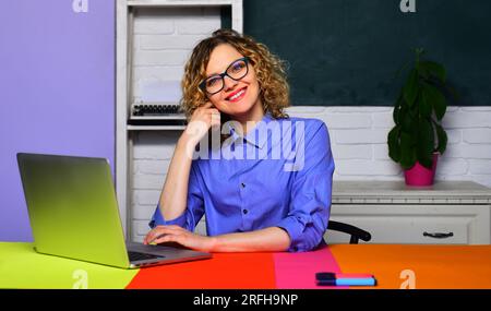 Lächelnder Lehrer mit Brille im Klassenzimmer. Studentin, die mit einem Laptop arbeitet und sich auf den Test oder die Prüfung vorbereitet. Hausaufgaben. Eine glückliche Schule Stockfoto
