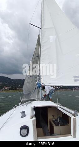 Ein Erwachsener Latino fährt ein Segelboot auf dem See mit Segeln, die als körperliche Aktivität, Sport und Hobby entwickelt wurden, um sich am Wochenende zu entspannen Stockfoto