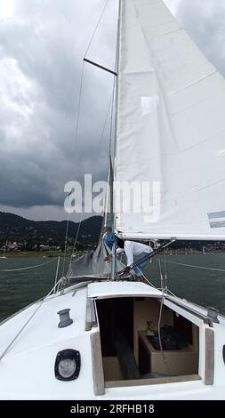 Ein Erwachsener Latino fährt ein Segelboot auf dem See mit Segeln, die als körperliche Aktivität, Sport und Hobby entwickelt wurden, um sich am Wochenende zu entspannen Stockfoto