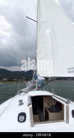 Ein Erwachsener Latino fährt ein Segelboot auf dem See mit Segeln, die als körperliche Aktivität, Sport und Hobby entwickelt wurden, um sich am Wochenende zu entspannen Stockfoto