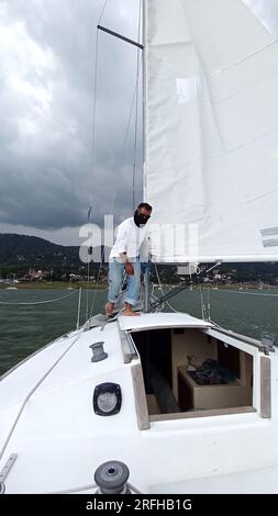 Ein Erwachsener Latino fährt ein Segelboot auf dem See mit Segeln, die als körperliche Aktivität, Sport und Hobby entwickelt wurden, um sich am Wochenende zu entspannen Stockfoto