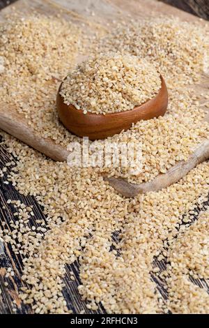 Roher, nicht gekochter Bulgur-Haferbrei, große Menge Getreide auf einem Holztisch, aus Weizenkörn Stockfoto