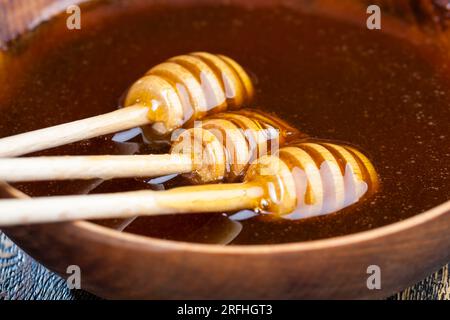 In Honig getaucht, der speziell aus Holz hergestellt wurde, ein hausgemachter Rohlöffel, süßer Bienenhonig und drei Holzlöffel, mit denen Sie Honig wi umfüllen und eingießen können Stockfoto